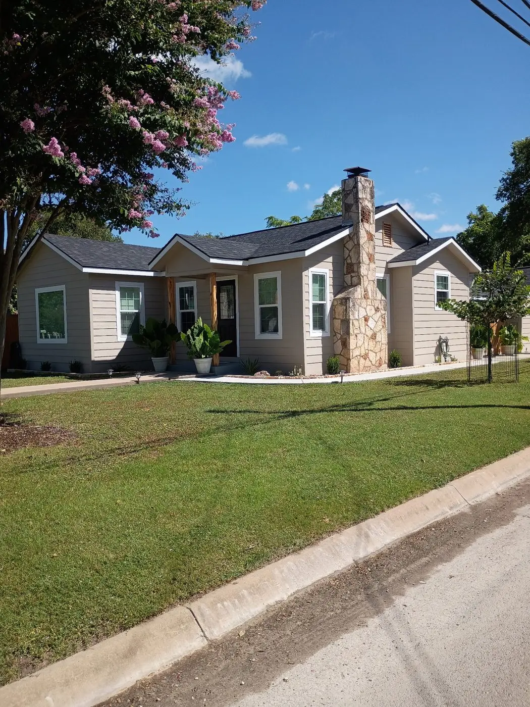 Completed Hill Country home with stone chimney and fresh siding, viewed from the street